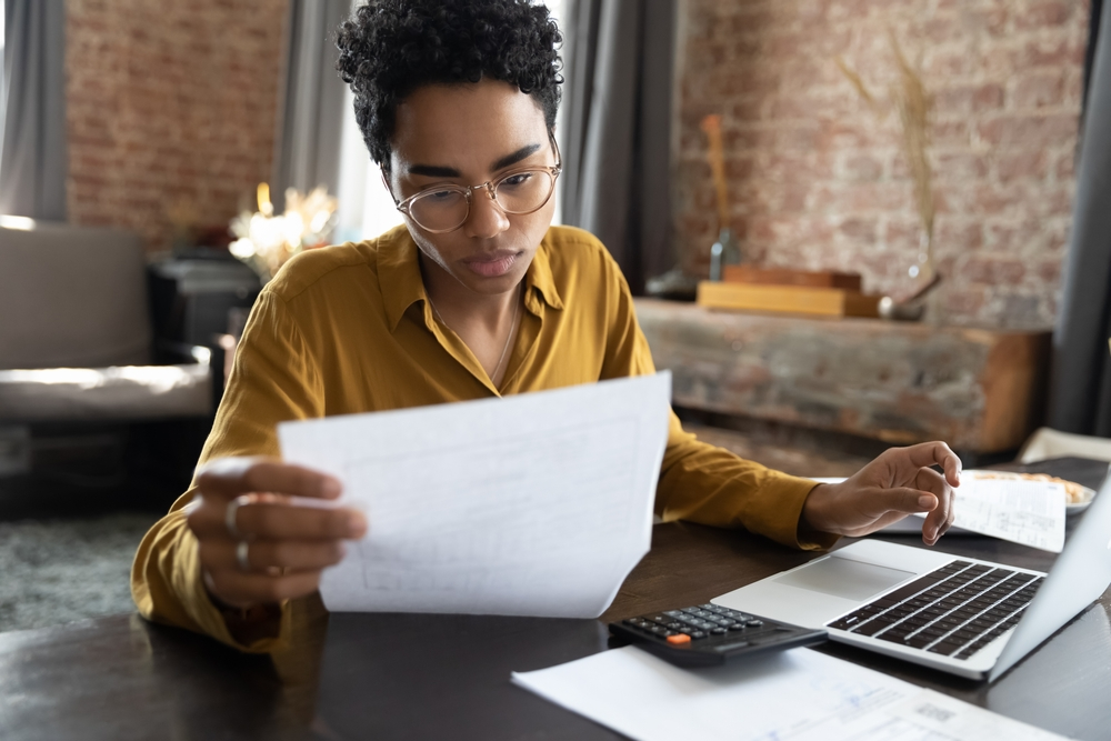 woman looking at paper documents with laptop and calculator