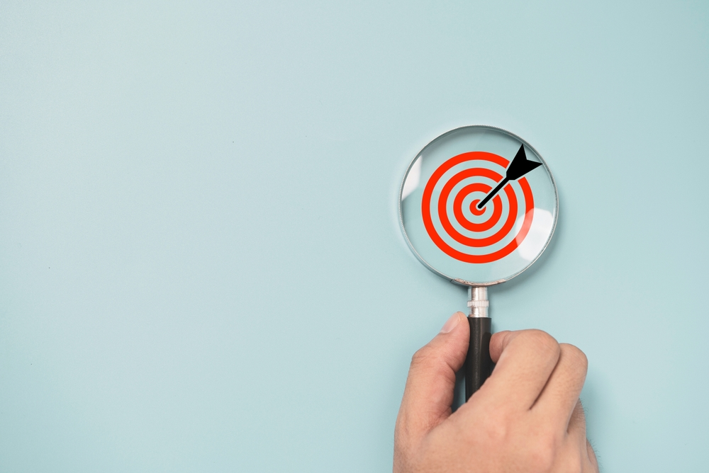 hand holding magnifying glass over red target with dart in the bulls-eye